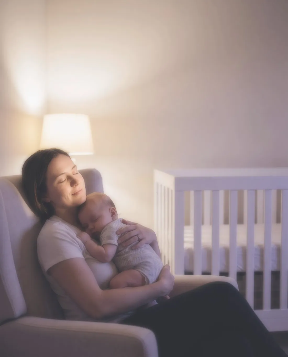 Mãe com o bebé a dormir ao colo, no quarto, ao fim do dia